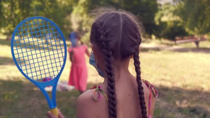 美丽的小女孩戴着医用面具和她的朋友打羽毛球。