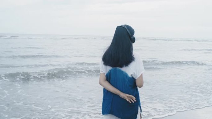 亚洲美女周末度假时，在海边的海滩上使用带耳机的智能手机听音乐。快乐的单人旅行概念。
