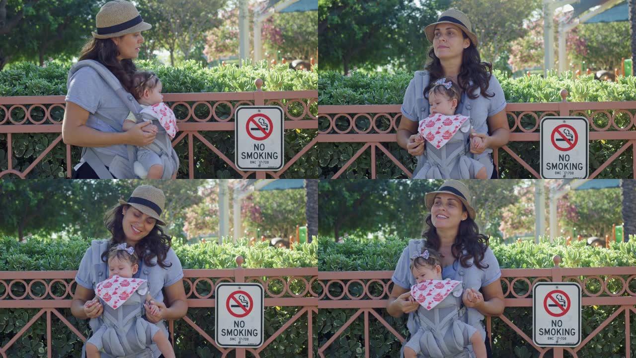 站在公园禁止吸烟标志旁边的提篮中的妇女和婴儿