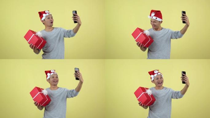 亚洲泰国男子用智能手机直播并在黄色背景上拿着红色礼盒