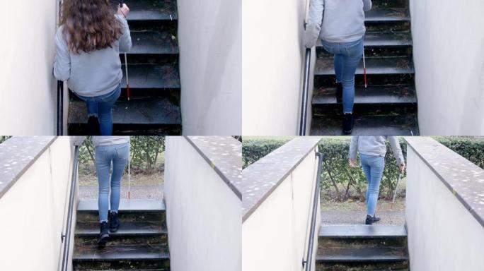 失明的年轻女子独自用棍子爬楼梯。自主，失明
