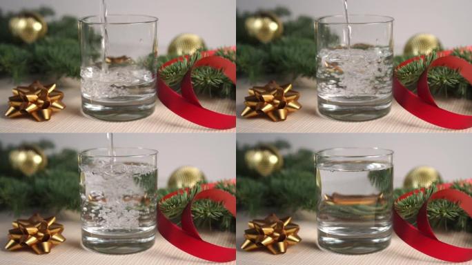 透明透明的液体气泡，倒入带有云杉树枝和圣诞节装饰品的桌子上的玻璃杯中