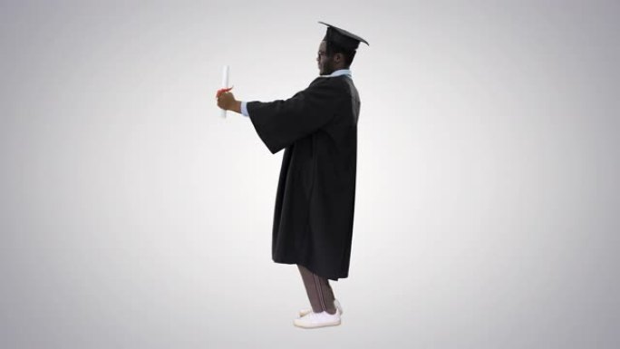 毕业长袍快乐的非洲裔美国男学生与渐变背景相机文凭合影
