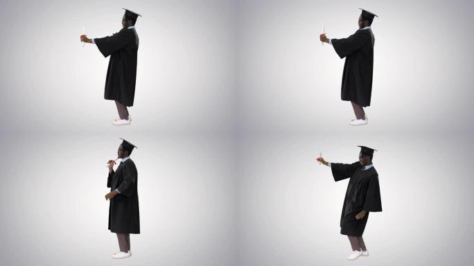 毕业长袍快乐的非洲裔美国男学生与渐变背景相机文凭合影