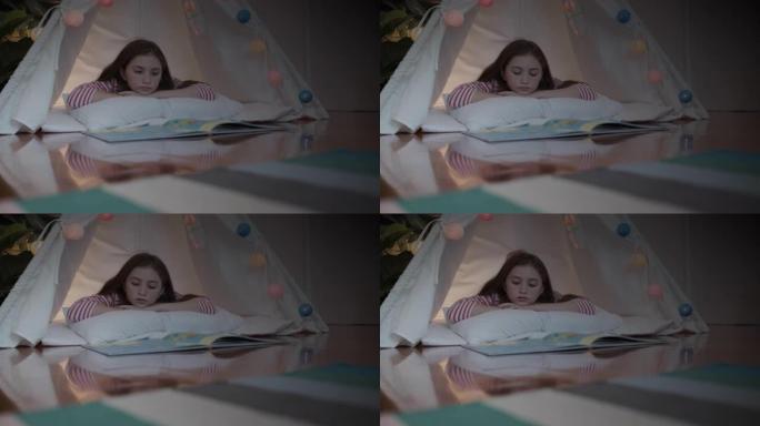 小女孩晚上在卧室的帐篷里躺下看书节日快乐主题