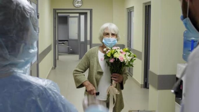 戴医用口罩的高级女患者手持鲜花出院