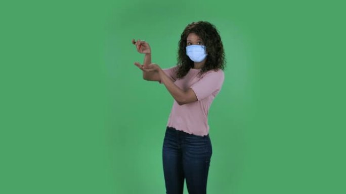 美丽的非裔美国年轻女子的肖像在医用防护口罩，为了防止冠状病毒的传播，手倒药。在工作室的绿色屏幕上燃烧