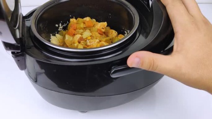 multicooker的宏视频。这个人打开锅，把盘子混合起来。从熟食中可以看到蒸汽。厨房烹饪自动化和