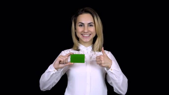 穿着白衬衫的年轻女商人手里拿着一张银行卡，表现得像。孤立的黑色背景。Chromakey绿卡