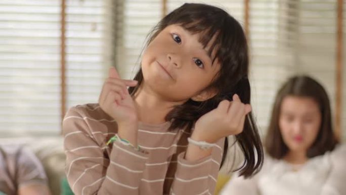 滑稽可爱的亚洲小女孩的肖像站在家里的客厅里，看着镜头摆姿势，带着滑稽、积极和快乐的情绪微笑。