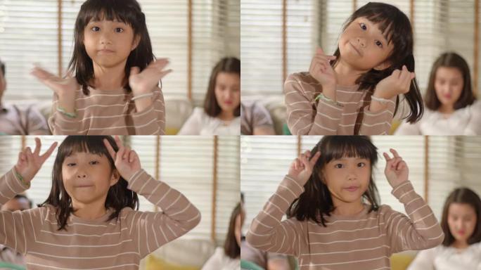 滑稽可爱的亚洲小女孩的肖像站在家里的客厅里，看着镜头摆姿势，带着滑稽、积极和快乐的情绪微笑。