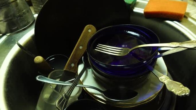厨房或餐厅水槽里一堆未洗的脏盘子。在家为家庭主妇工作。水槽里有脏盘子、杯子、勺子、叉子和一把刀。洗脏