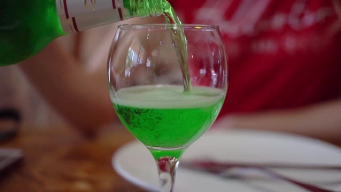 餐馆里的一名妇女将绿色的龙蒿饮料倒入玻璃杯中。咖啡馆的晚餐。慢动作