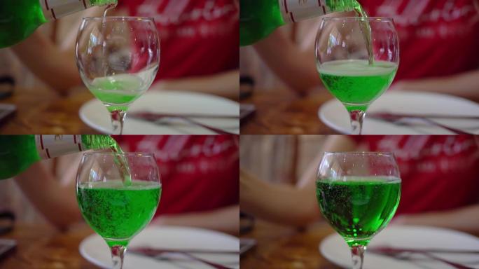 餐馆里的一名妇女将绿色的龙蒿饮料倒入玻璃杯中。咖啡馆的晚餐。慢动作