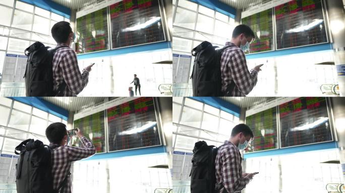 COVID 19期间的旅行和运输。戴着防护面具的男子站在机场航站楼附近的出发和到达时间电子板处时使用