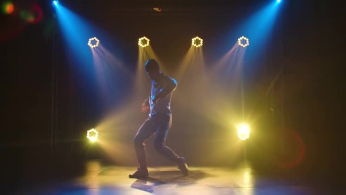专业表演霹雳舞，由时尚的男性街头舞者表演的嘻哈。在舞台灯光的背景下，一个穿着运动服和运动鞋的男人的轮