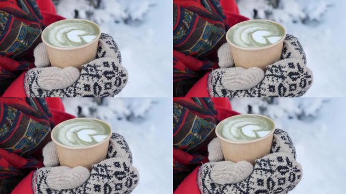 在户外下雪的冬天早晨，手握着一杯热腾腾的热咖啡或茶，在针织连指手套中收起手