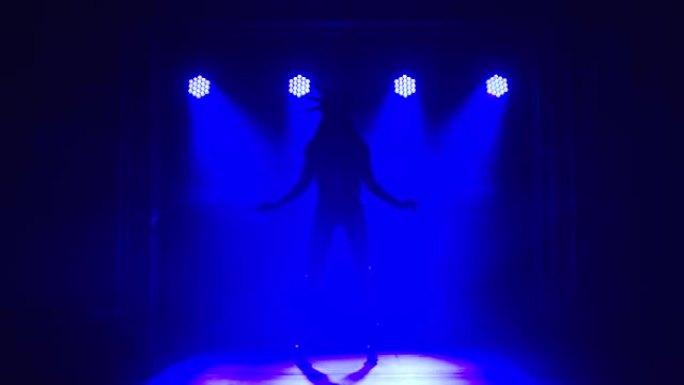 穿着性感西装的迷人黑发女郎美国自由女神像在黑暗的工作室里跳舞，烟熏和蓝色霓虹灯。穿着高跟鞋的长腿美女