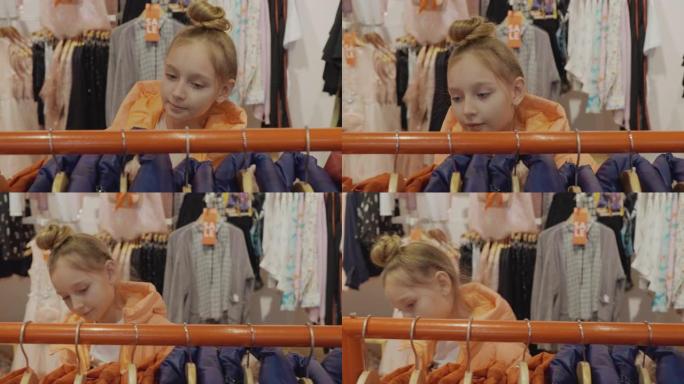 可爱的少女在时尚精品店里看着穿着时尚衣服的衣架