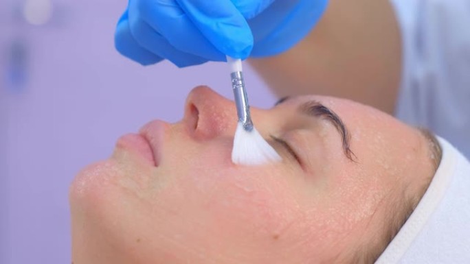 美容师在语音电泳手术前在女性脸上涂抹凝胶。