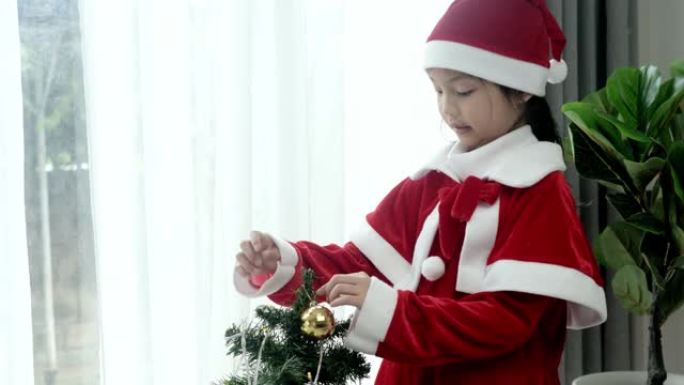 亚洲女孩穿着圣诞老人的服装，在家装饰圣诞树，生活方式概念。