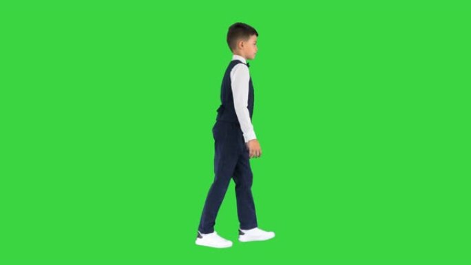 一个穿着马甲打着领结的小男孩走在绿色屏幕上，眼睛直视前方