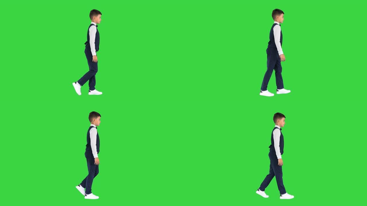 一个穿着马甲打着领结的小男孩走在绿色屏幕上，眼睛直视前方