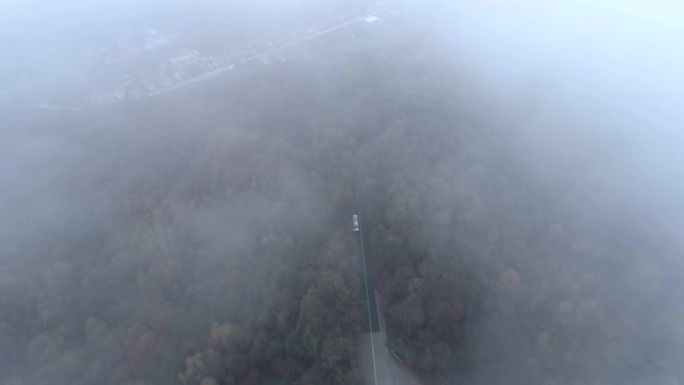白色卡车在危险的迷雾森林路上行驶的俯视图。无人机在雾蒙蒙的道路上追逐白色公共汽车
