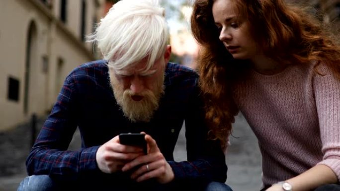 一对夫妇坐在城市街道的台阶上一起看手机
