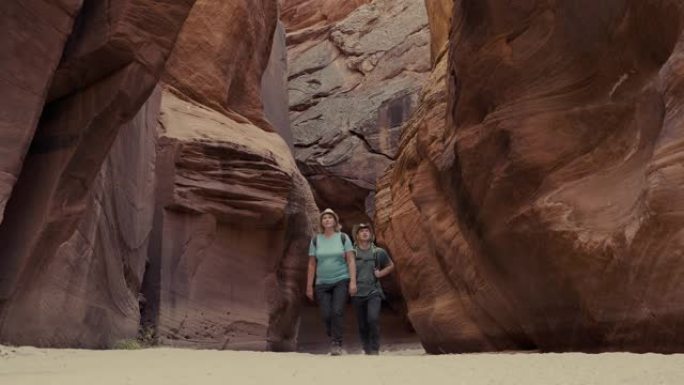 徒步旅行者沿着带有弯曲岩石的深洞槽峡谷中的沙质河床徒步旅行