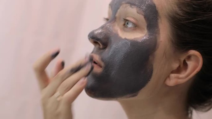 年轻女子正在脸上涂上粘土灰色面膜，特写侧视图。