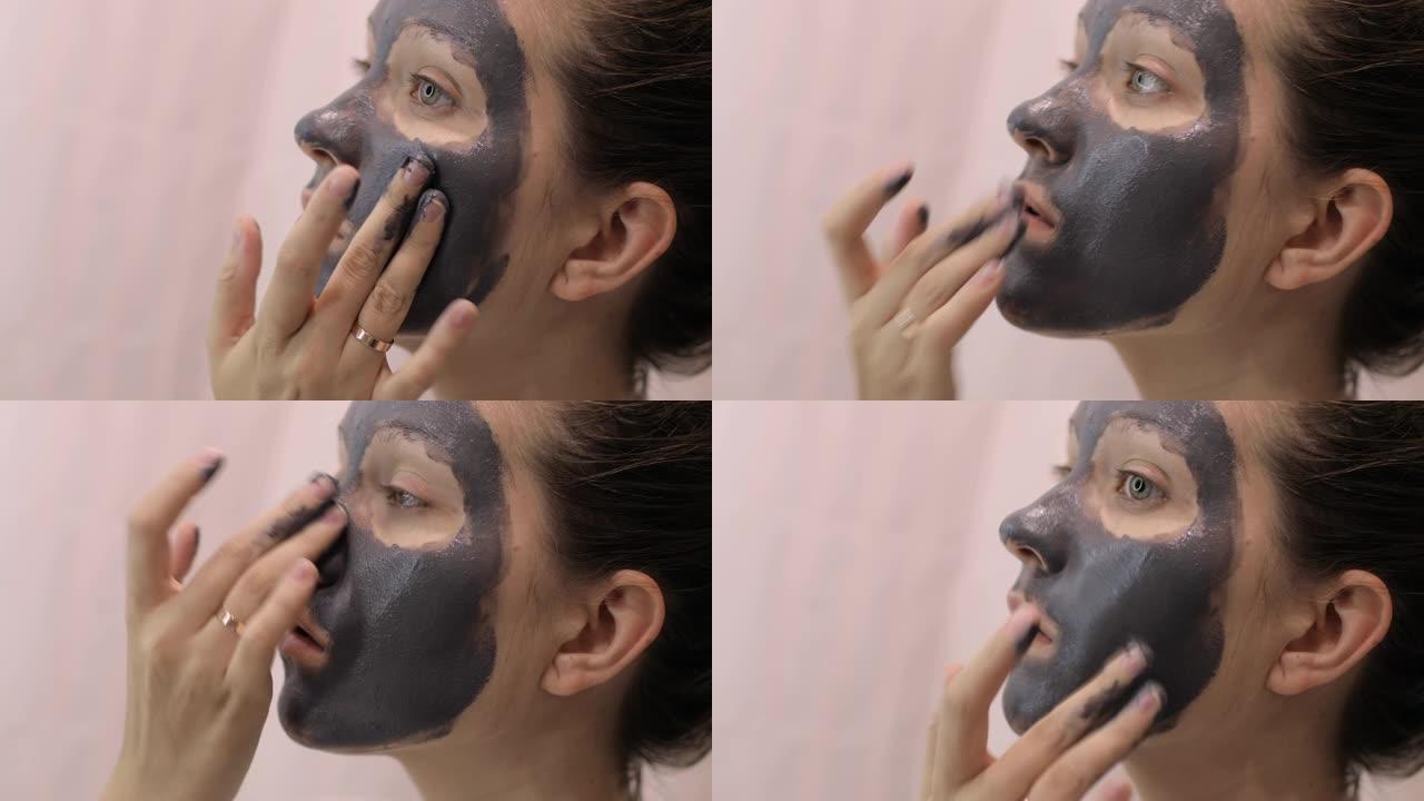 年轻女子正在脸上涂上粘土灰色面膜，特写侧视图。