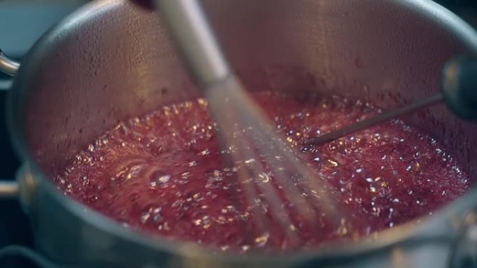 女人用小搅拌器搅拌煮沸的红莓焦糖