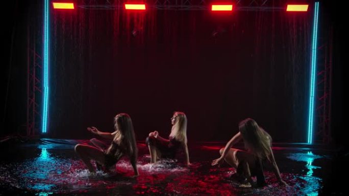 三位苗条的女舞者在落水的背景下优雅地在雨水坑中跳舞。慢动作