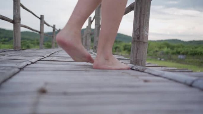 慢动作特写女性赤脚行走木桥，背景是绿色的稻田和高山，非城市场景触摸当地自然，人类健康健康，撤退宁静