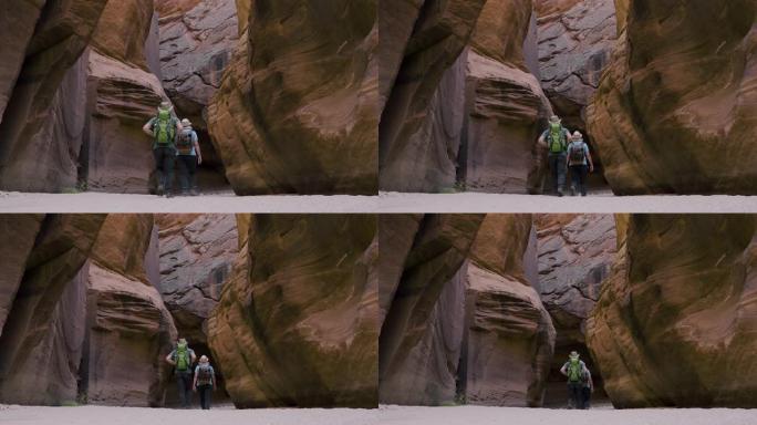 徒步旅行者沿着带有弯曲岩石的深洞槽峡谷中的沙质河床徒步旅行
