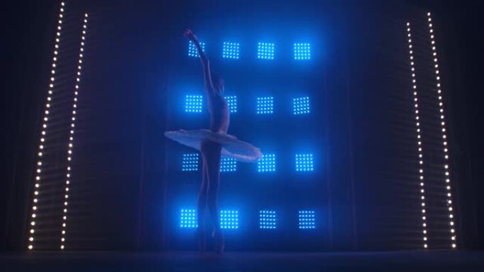 漂亮的芭蕾舞演员优雅地跳舞。演出前的芭蕾彩排。芭蕾舞演员穿着舞台服装舞步。剪影。带烟雾和蓝色霓虹灯的