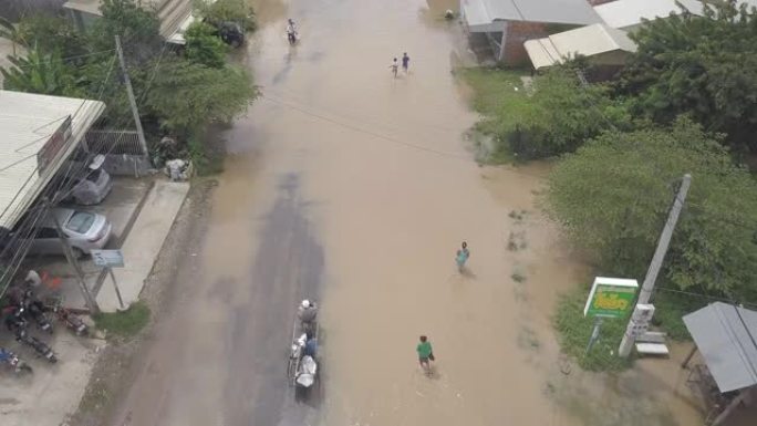 骑摩托车的人和村民在洪水泛滥的街道上走过小镇的空中头顶