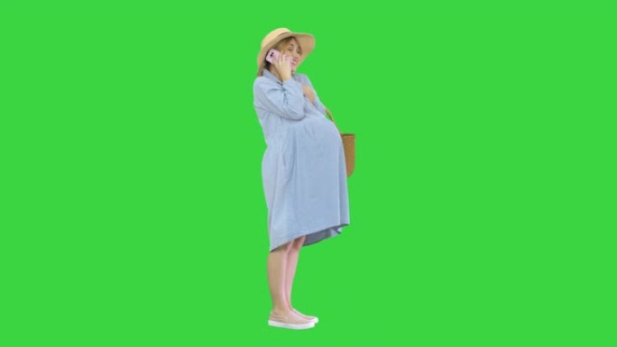 孕妇在夏天在绿屏上站着并通过电话交谈，色键