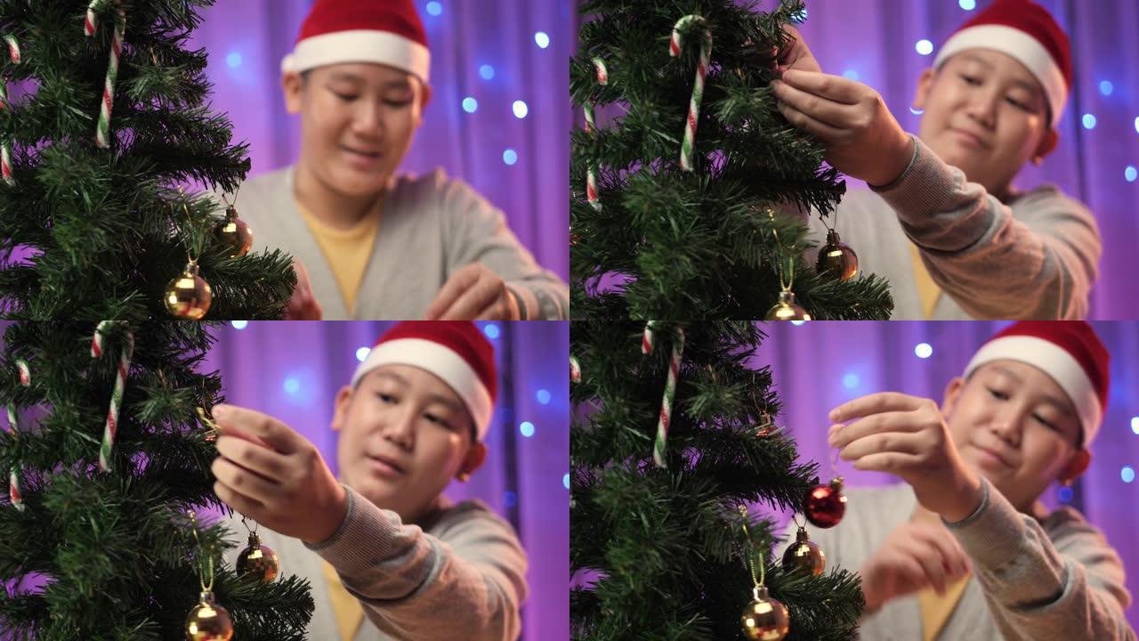 亚洲男孩戴着圣诞老人的帽子，在家里的圣诞树上悬挂装饰品，准备概念。