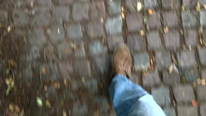 穿着牛仔裤和鞋子的腿沿着一条古老的鹅卵石小径行走
