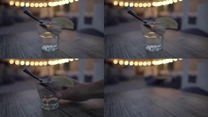 一种透明颜色的冷酒精饮料，在低矮的玻璃杯中，配以柠檬片和两根吸管，放在餐厅的木桌上，周围是黑暗而复古