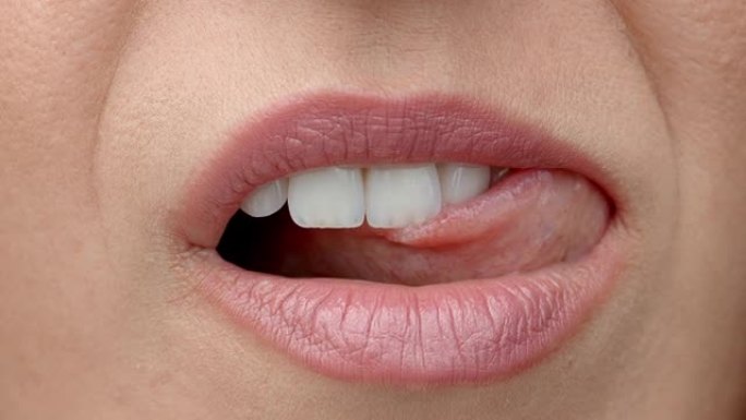 女人舔她的嘴唇。温柔的女性舌头舔美丽的洁白牙齿。