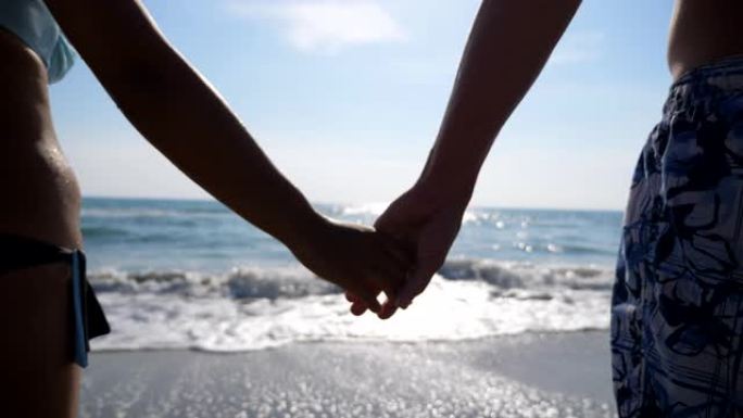 男女双手在美丽的海景背景下互相牵着。一对恋人站在海滩上，携手共进，欣赏风景。在暑假一起度过时光。