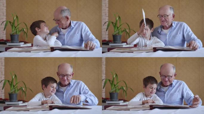 戴着眼镜的老人和他的孙子一起欣赏快乐的回忆，看着一张家庭相册坐在房间的桌子旁