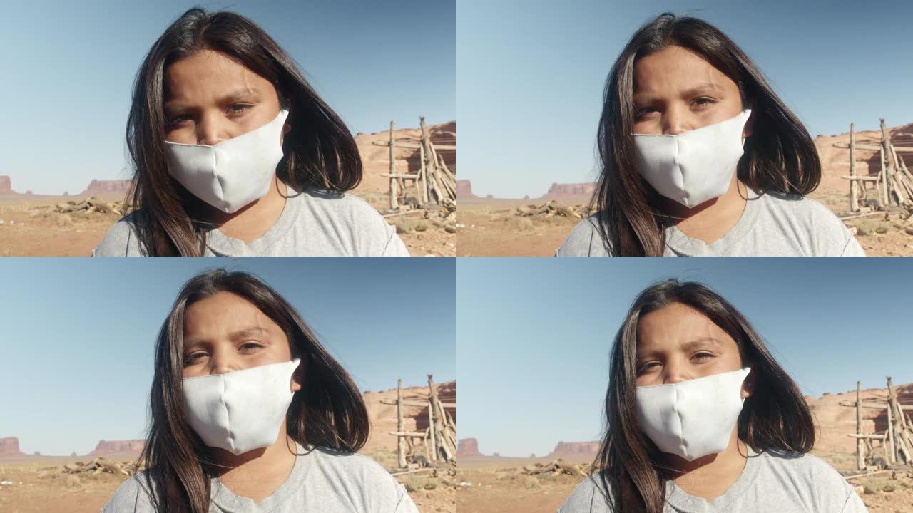 亚利桑那州北部沙漠中的一个年轻的纳瓦霍裔印第安男孩看起来很严肃，穿着新型冠状病毒肺炎的面具，背景是纪