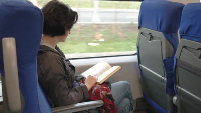白人妇女坐在窗边的火车上看书，火车停在平台上