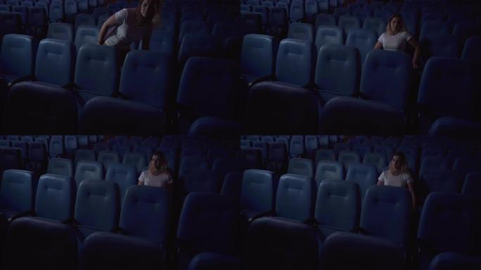 一个女人独自在空荡荡的电影院看电影。电影院