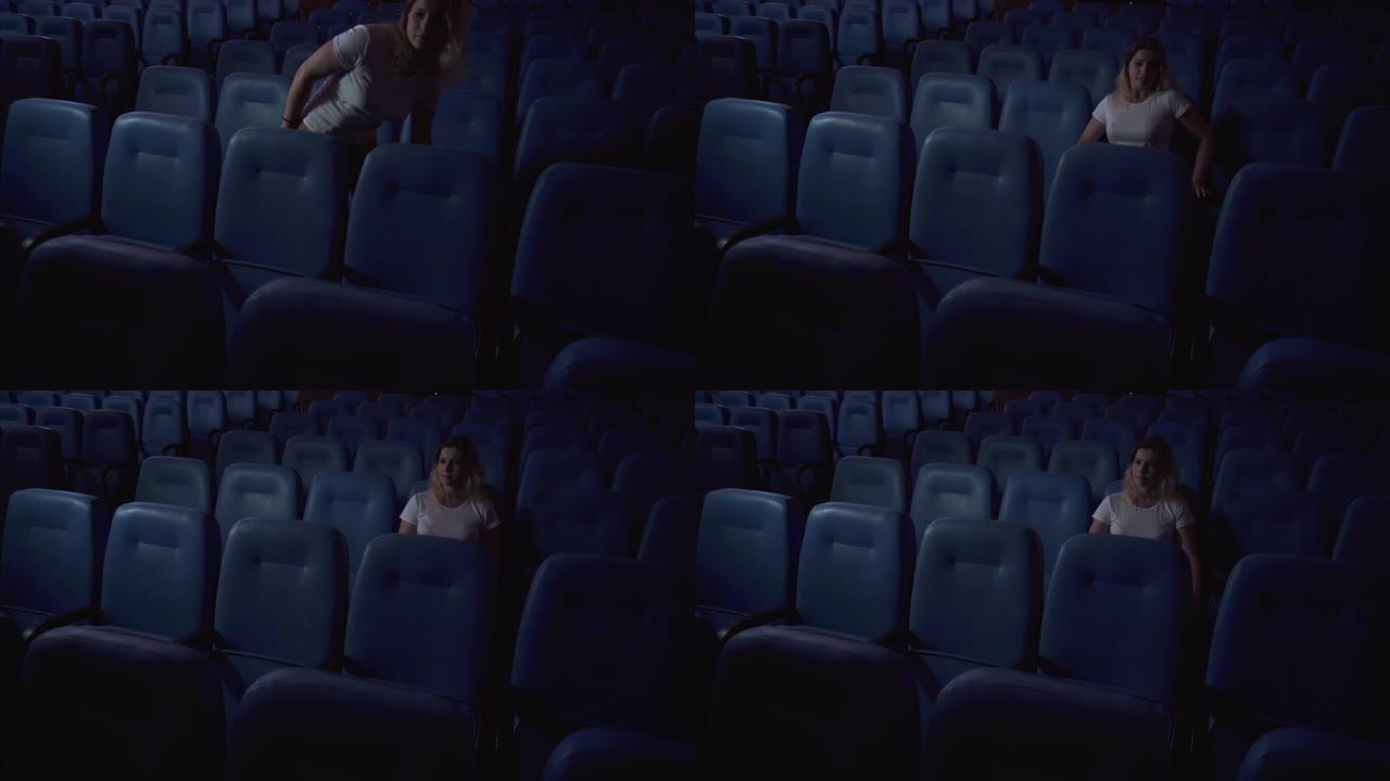 一个女人独自在空荡荡的电影院看电影。电影院