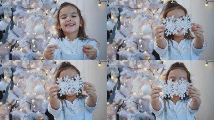 特写4k视频，微笑的女孩，小雪公主，在圣诞树附近，在白色背景上，向相机延伸了两片人造雪花。